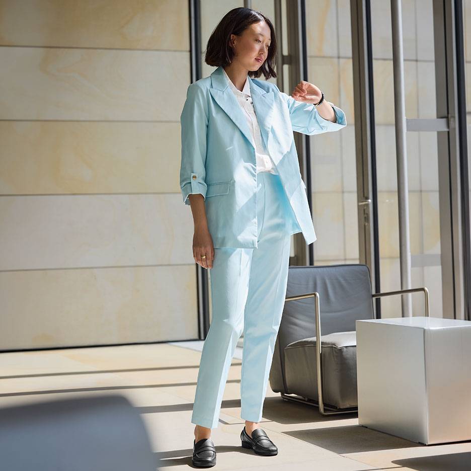 Woman in a light blue suit with a blazer and trousers, wearing black loafers.