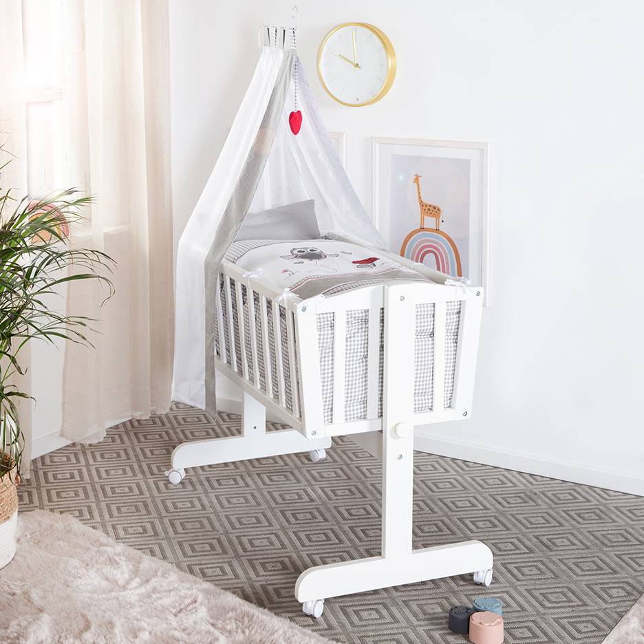 White baby crib with canopy and cute bedding patterns, in a room with a rug.