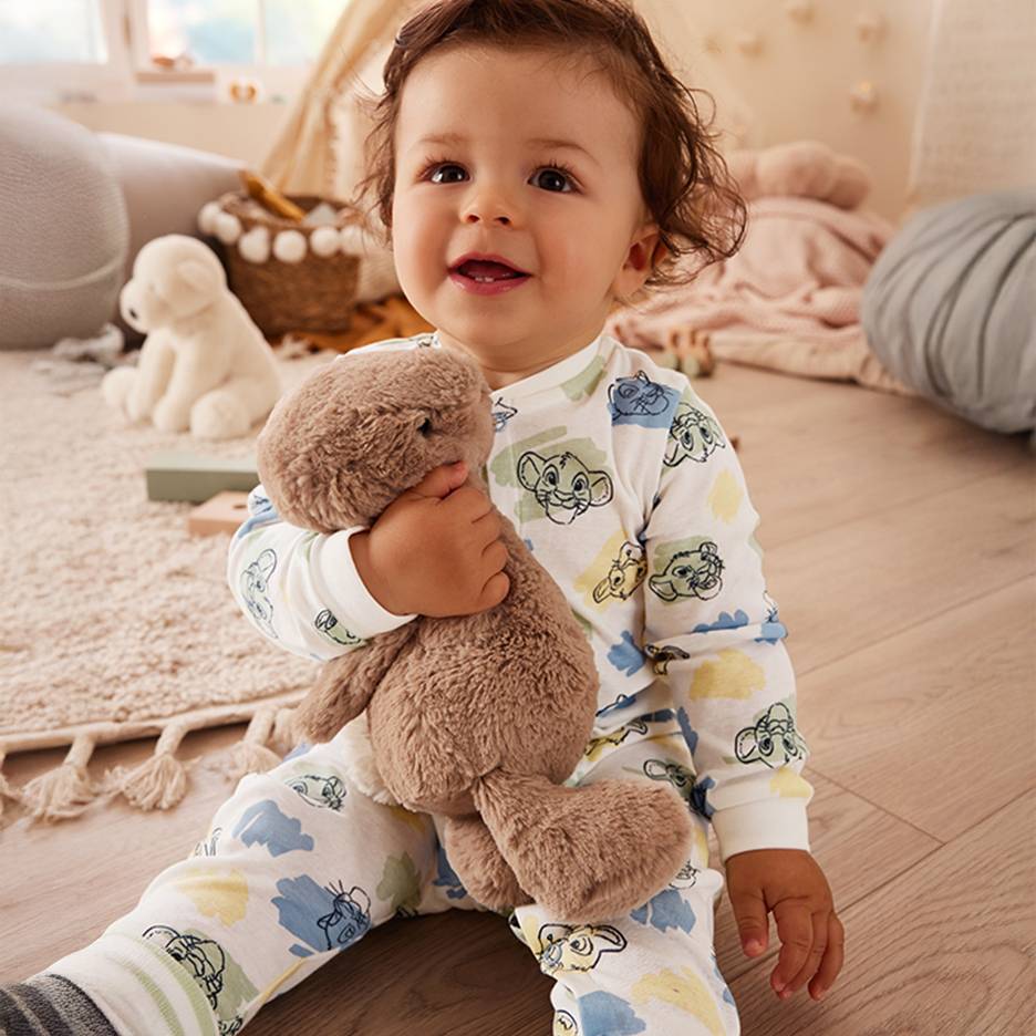 Happy baby in Lion King pajamas holding a brown plush toy.