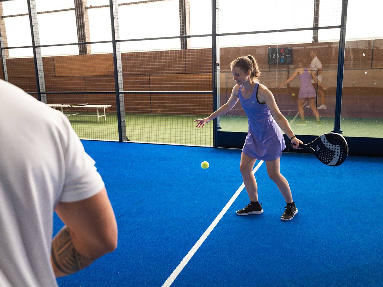 Woman playing padel, holding a racket and looking at the ball on a blue court.