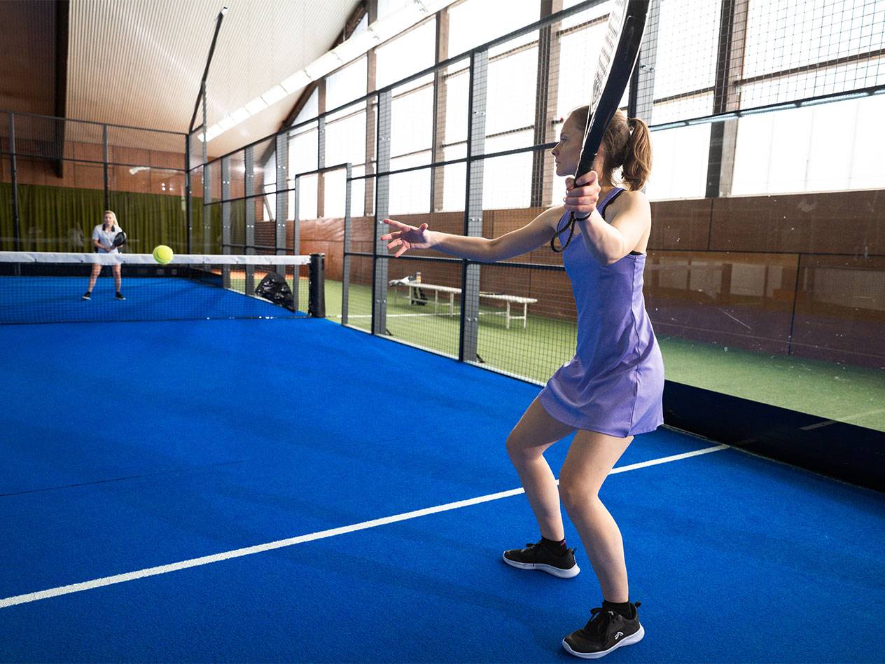 Woman in a purple sports dress playing padel on a blue court.