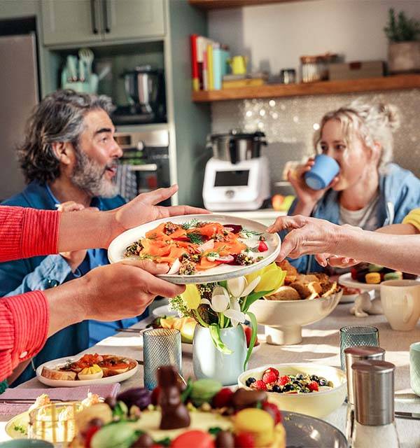 Family sharing a meal with salmon, desserts, and fresh fruit on a dining table.