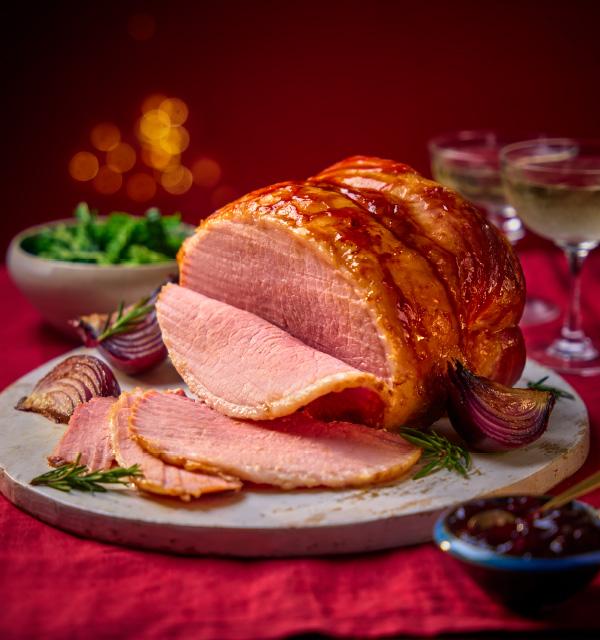 Glazed roast ham sliced on a serving board with red onions and festive table settings.