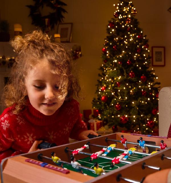A child playing with a wooden tabletop foosball game in front of a Christmas tree.