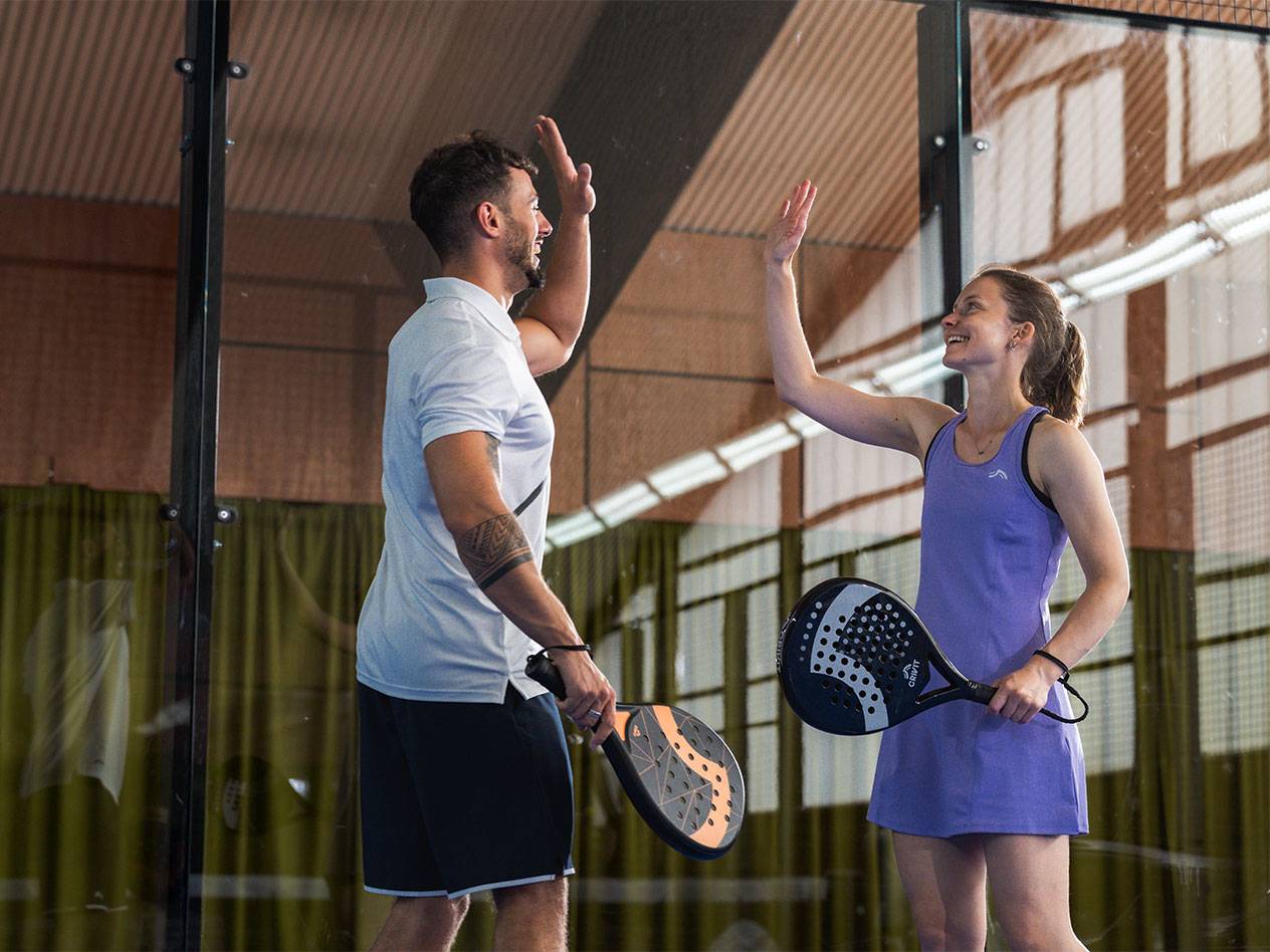 Two padel players in sportswear high-fiving on the court.