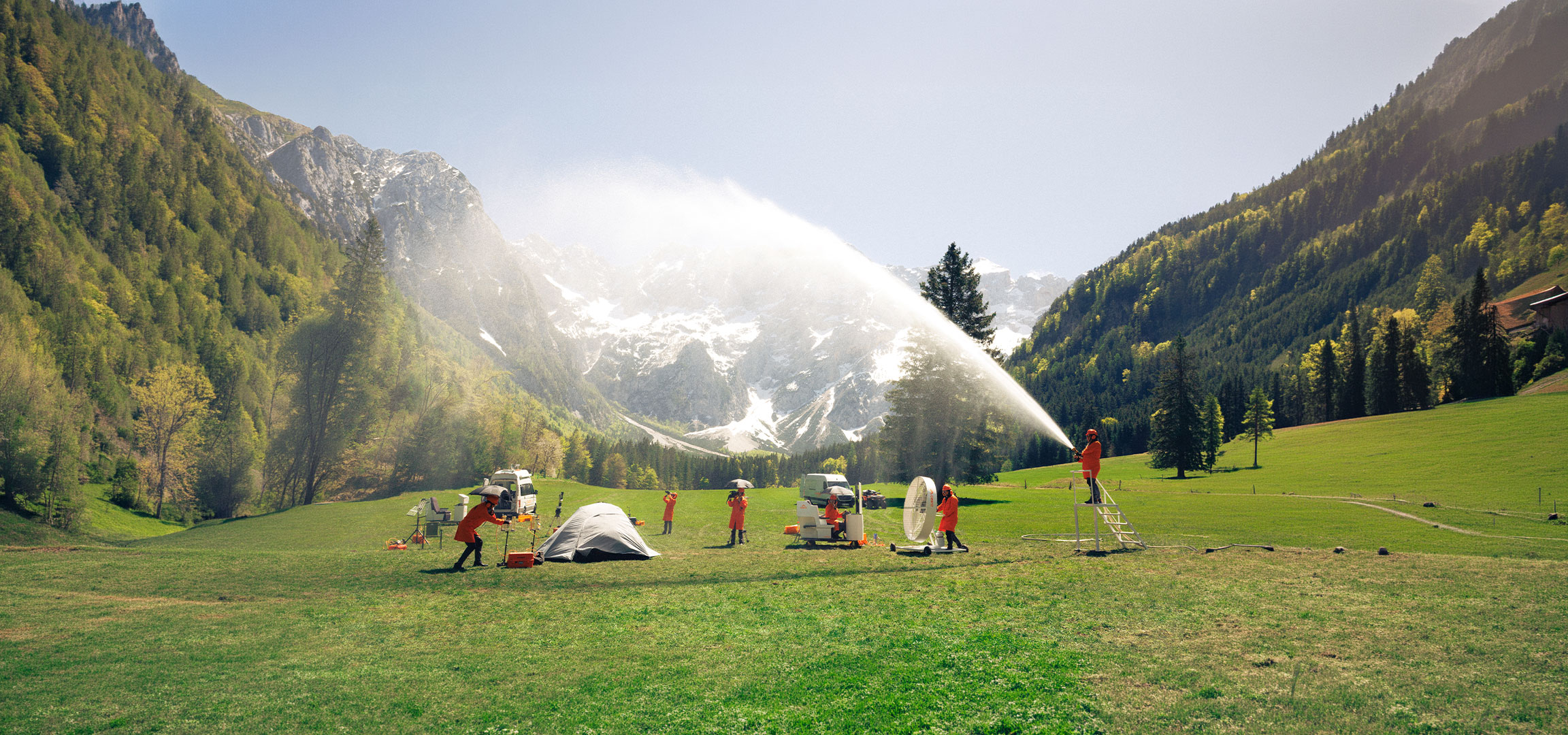 aiLabeling.aiLabelForImageAltText: People in orange protective suits testing camping and outdoor equipment in a meadow.