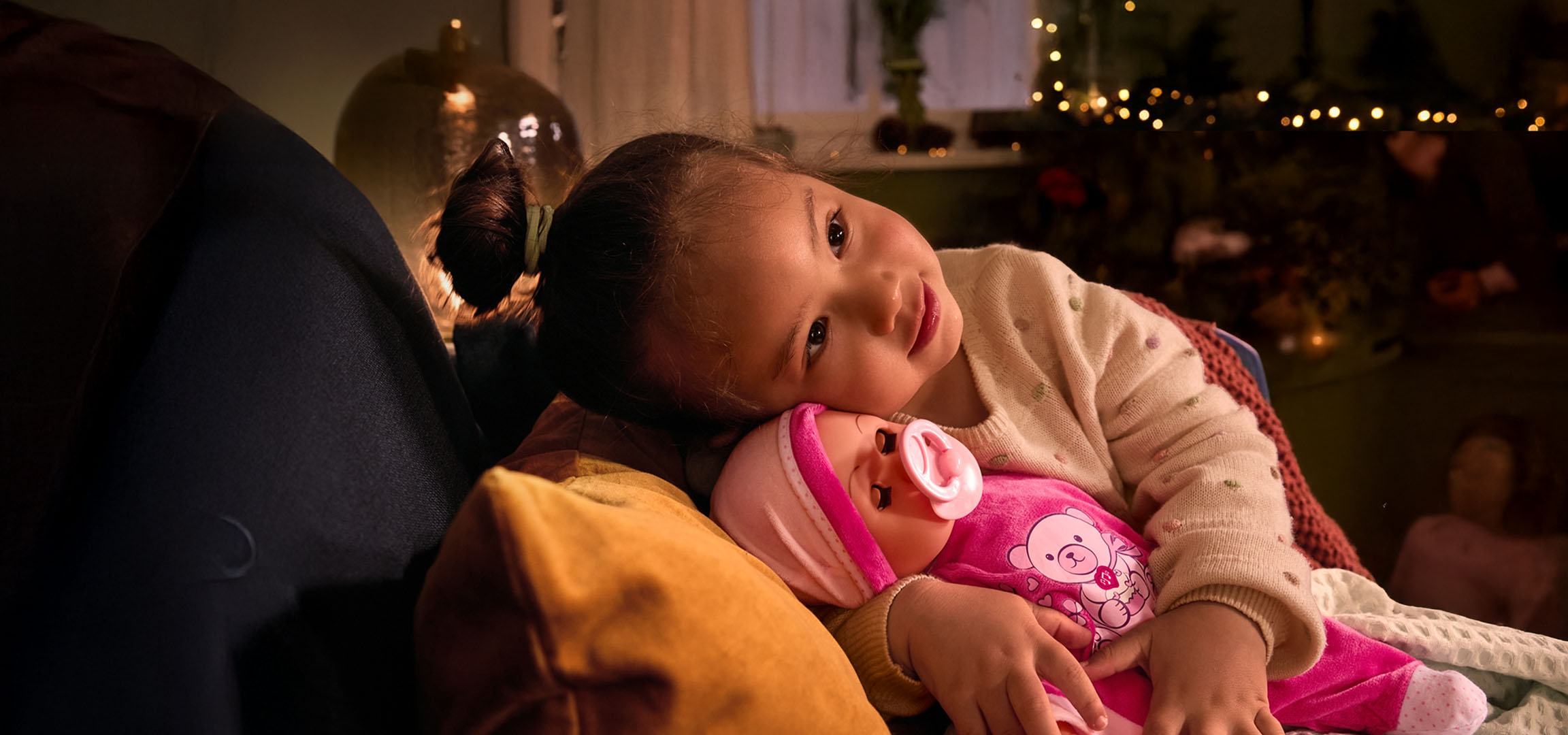 Girl with a doll and pacifier, cozily nestled on a pillow.