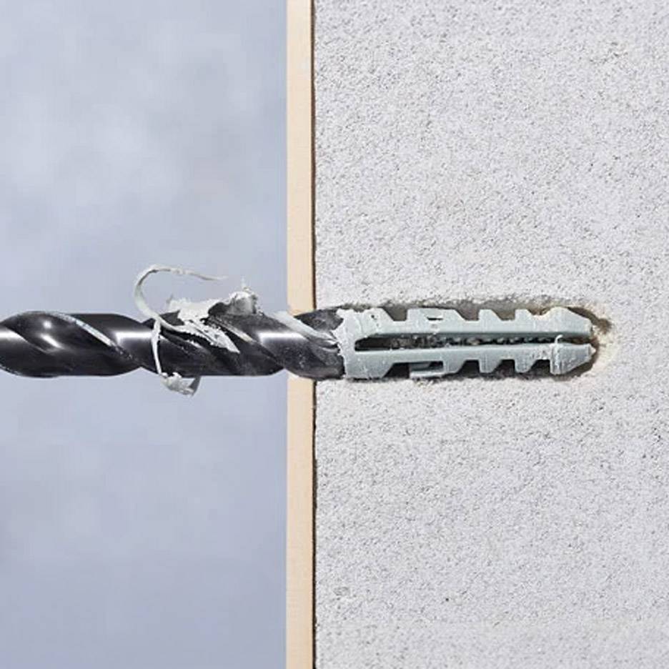 Drill bit drilling into a wall with a fixing plug.