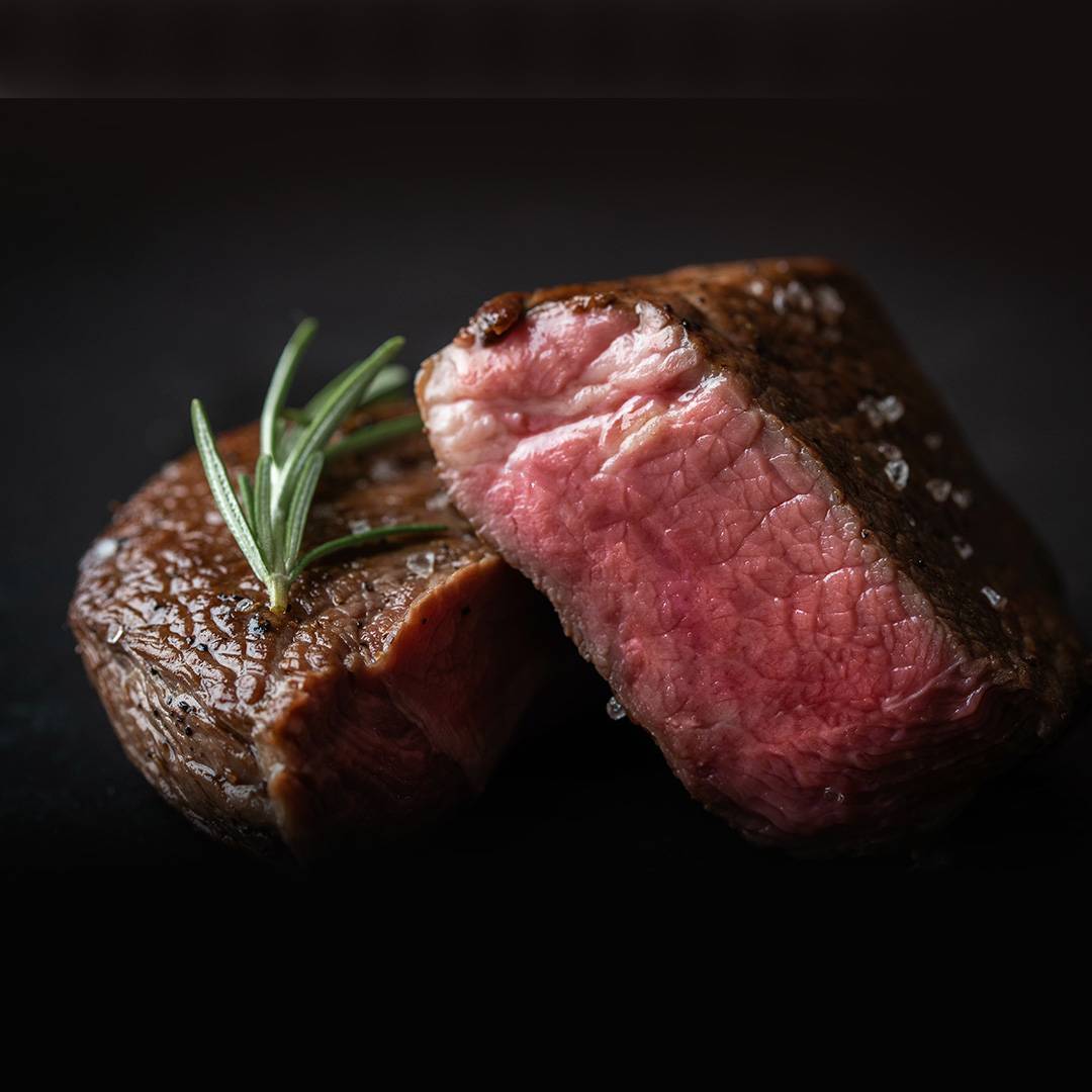Two perfectly cooked steaks, one cut open to reveal a pink, juicy interior, garnished with rosemary.