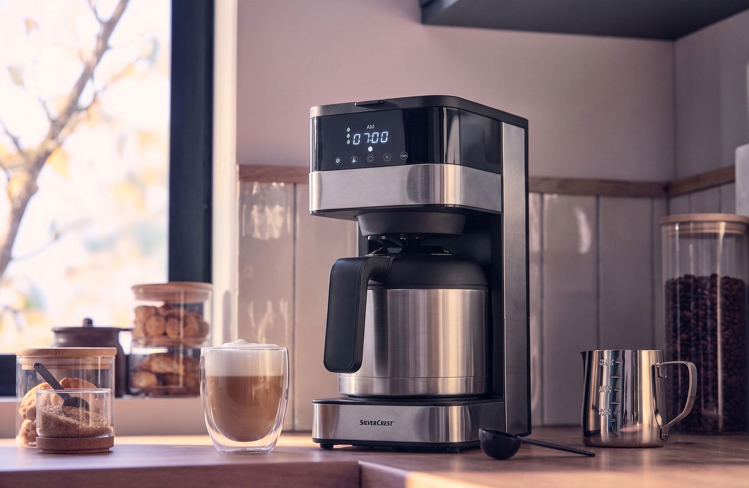 Coffee maker with thermal carafe and digital display showing 07:00 AM, with a cup of latte coffee.
