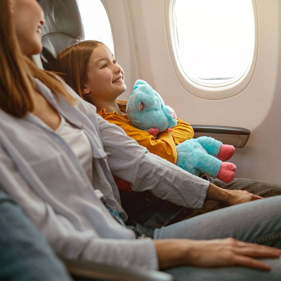 A child with a plush toy looking out an airplane window next to an adult.