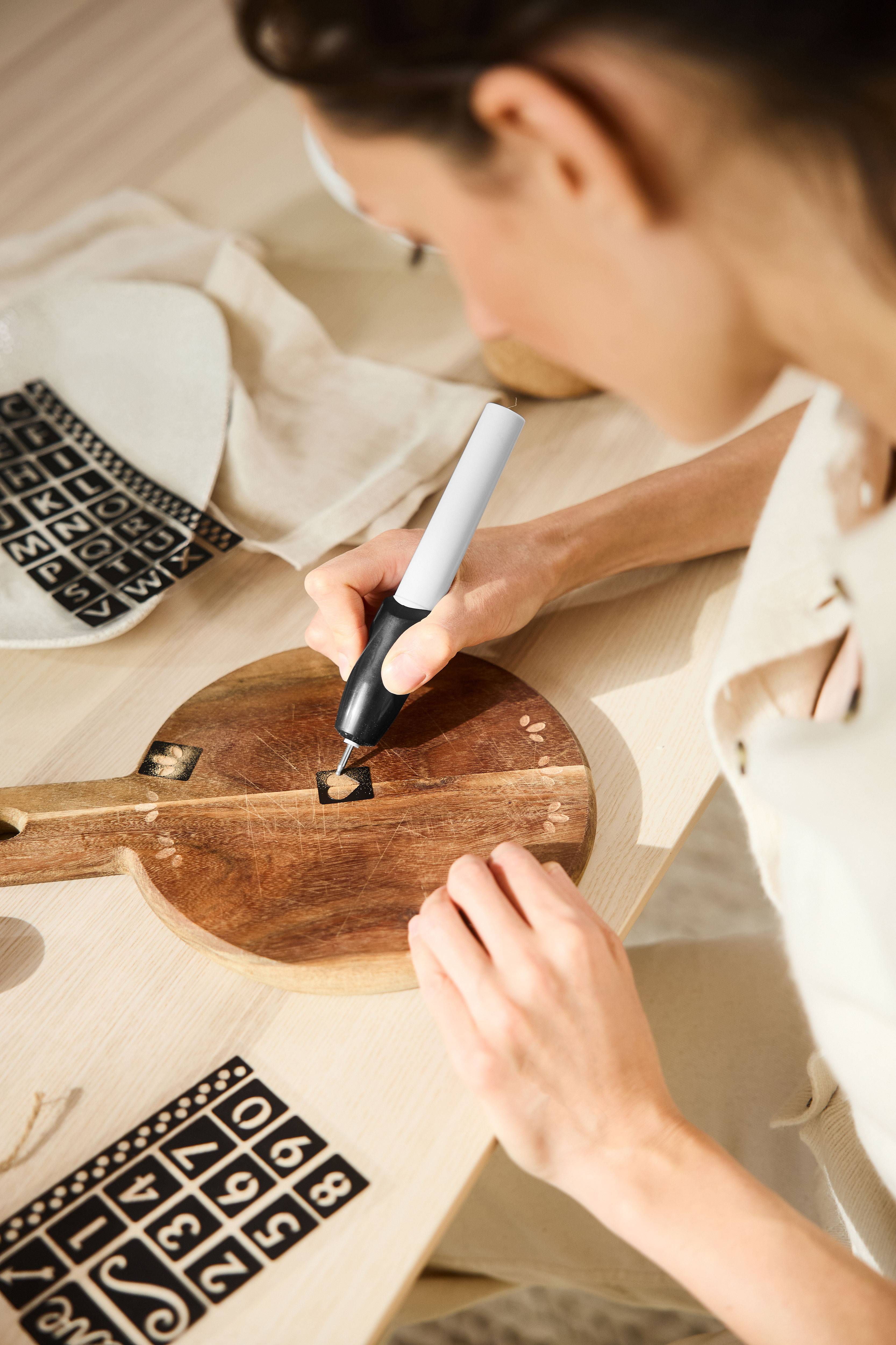 Woman engraving a wooden board using an engraving pen and stencils.