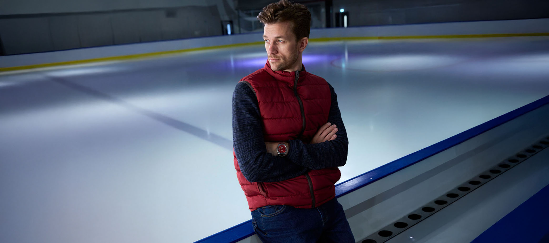 Man in a red vest and blue sweater standing on an ice rink