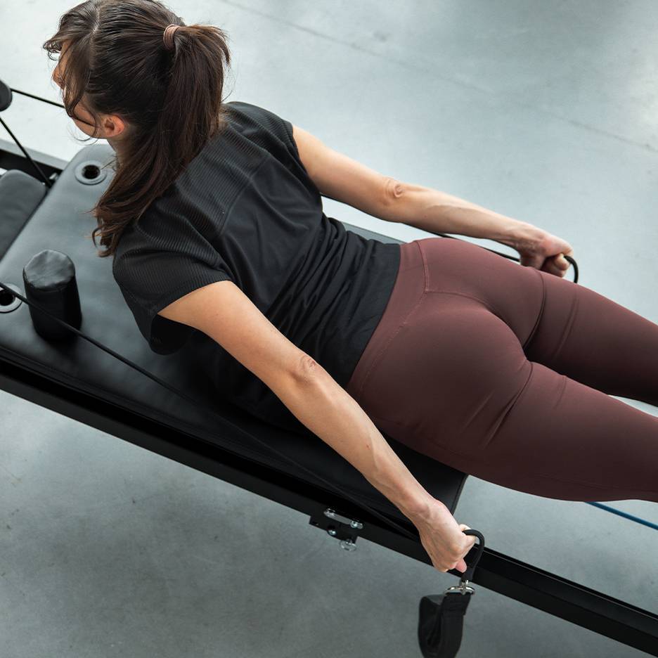 Woman exercising on a Pilates machine with resistance bands, wearing activewear.