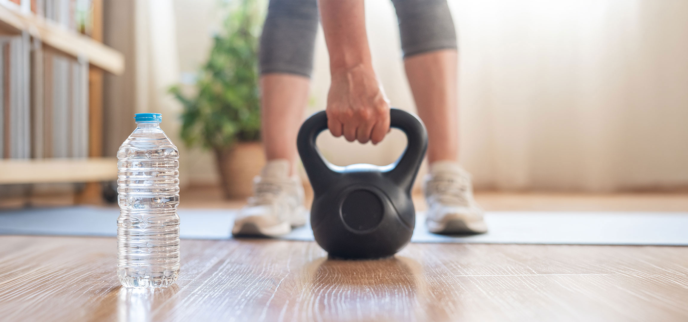 aiLabeling.aiLabelForImageAltText: Woman prepares to work out with a kettlebell and water bottle on a yoga mat.