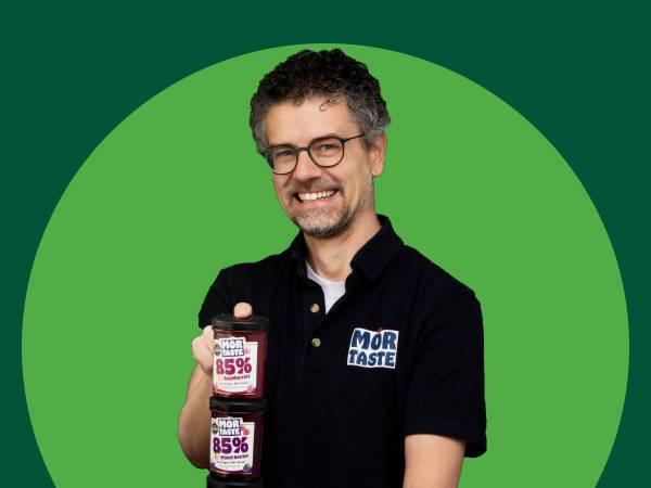 Smiling man in glasses holding two jars of fruit spread with 85% fruit content.