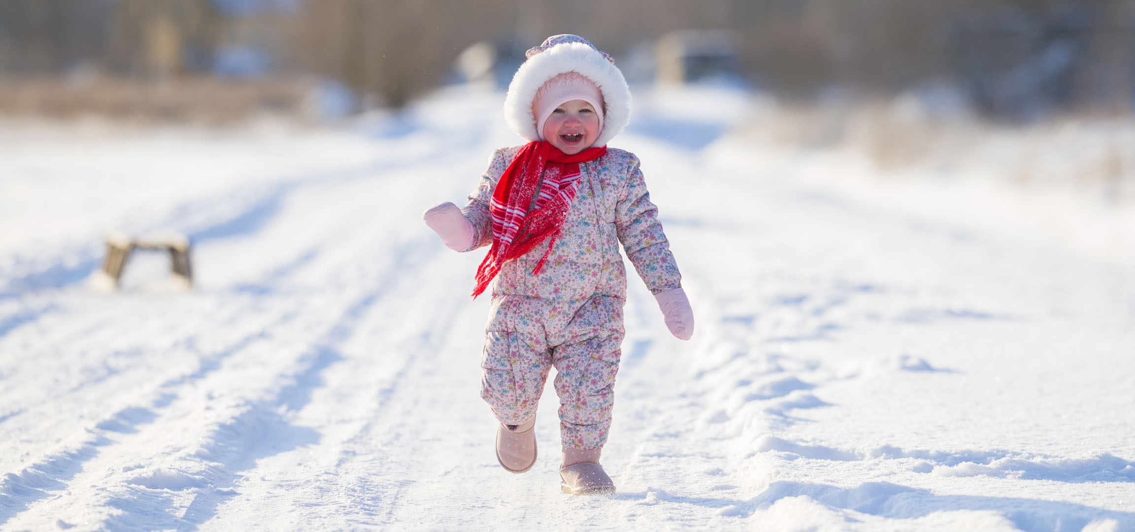 Joyful little girl in a winter jumpsuit and scarf running on a snowy path.