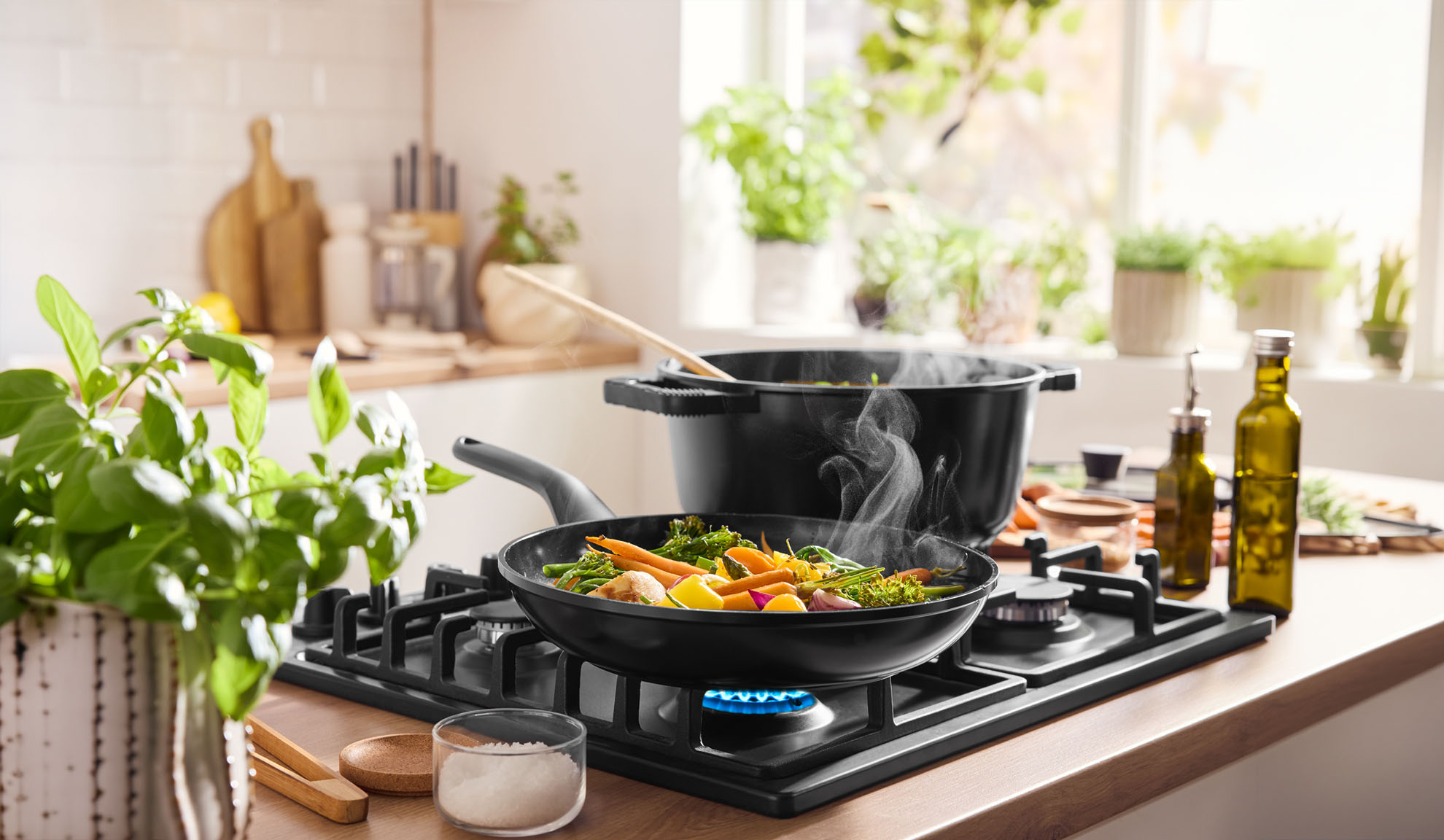 Steaming vegetables cooking in a pan and pot on a gas hob in a bright kitchen.