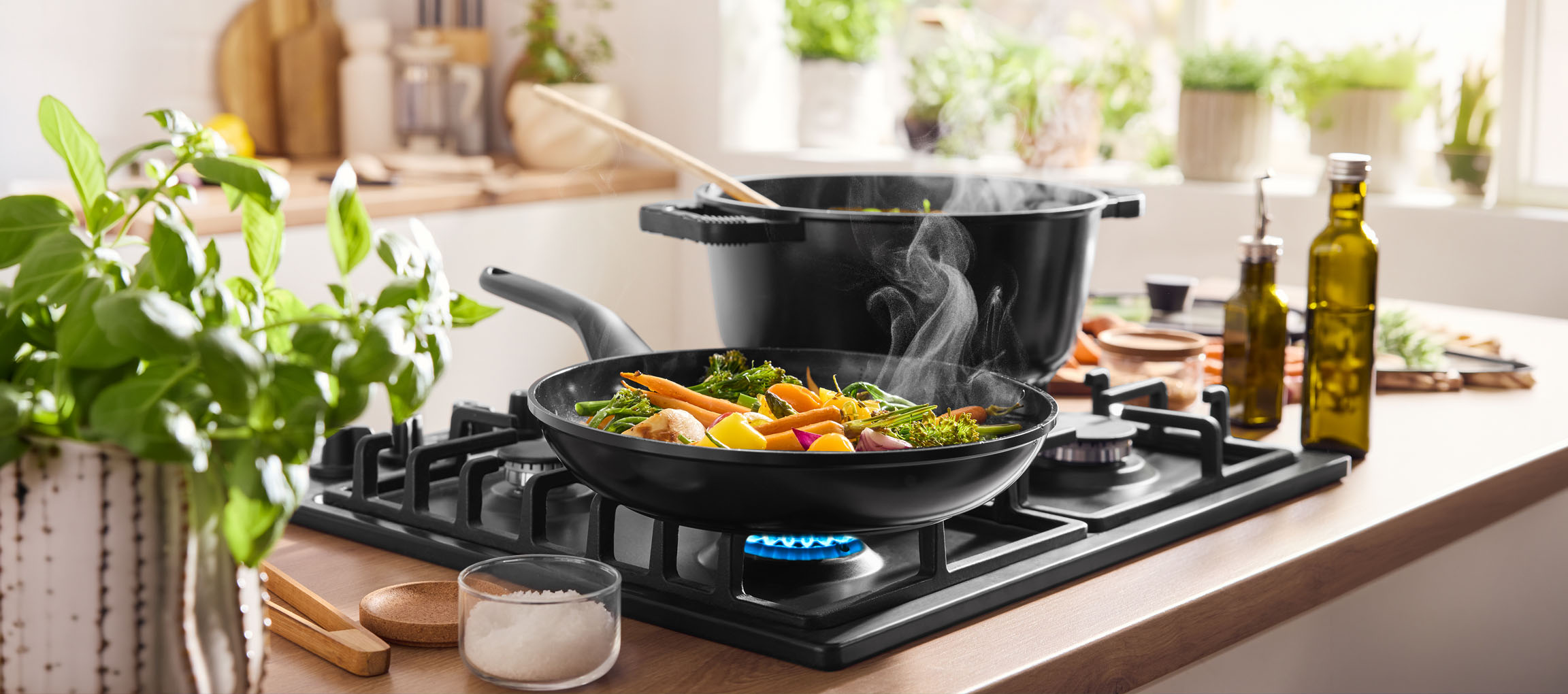 Cooking vegetables in a pan on a gas hob, with a pot and olive oil nearby.