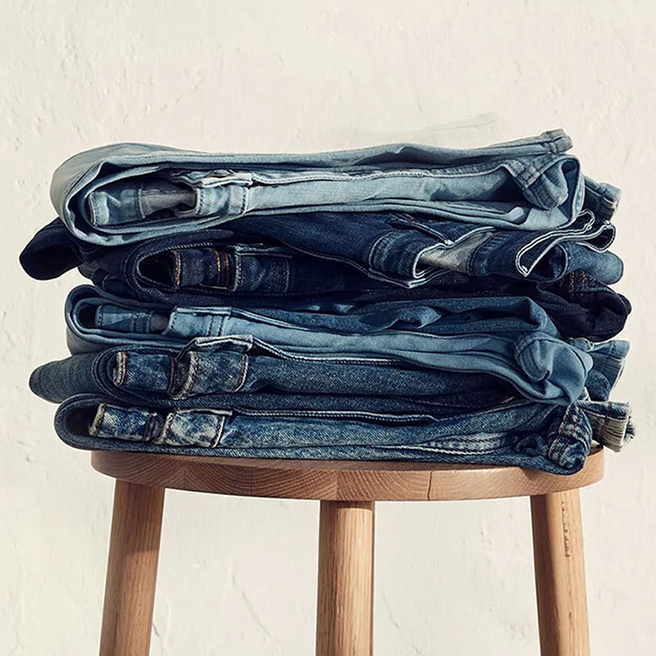 Uma pilha de jeans em vários tons de azul em um banquinho de madeira.