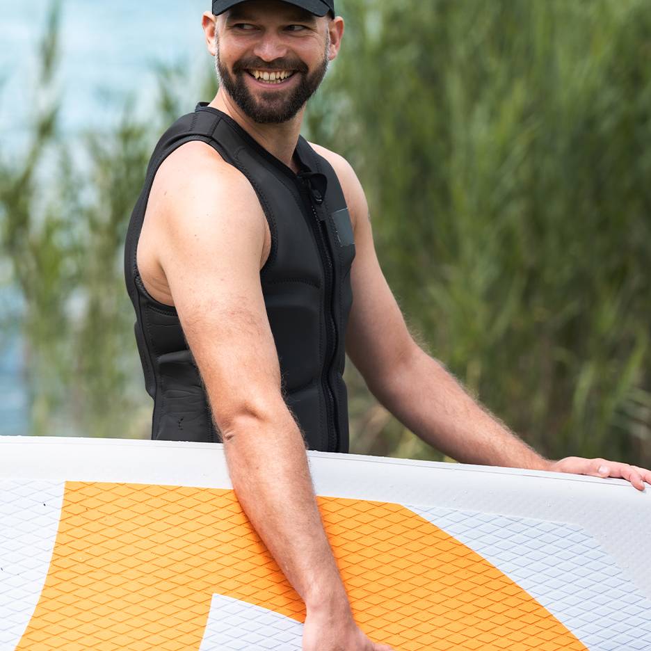 Smiling man in black life vest holding a paddleboard.