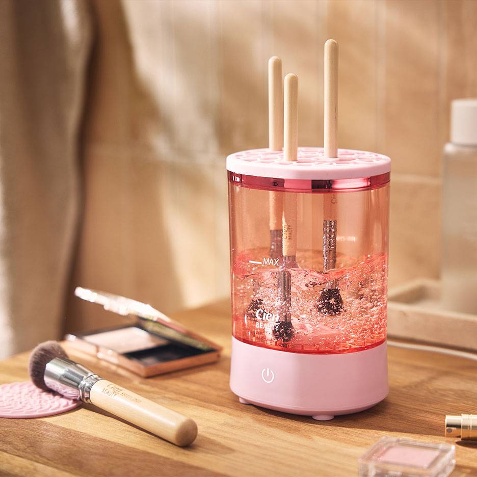 Pink makeup brush cleaner with brushes in bubbly water.