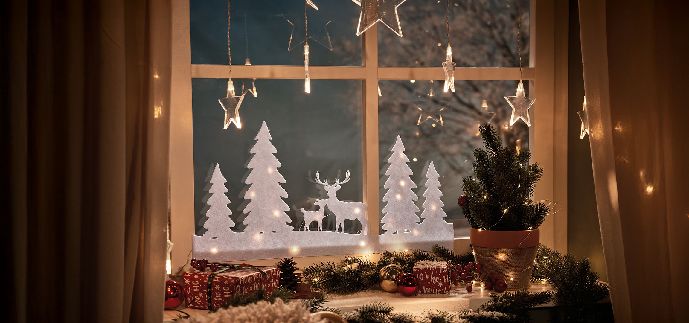 Christmas window decoration with trees, deer, gifts, and lights.