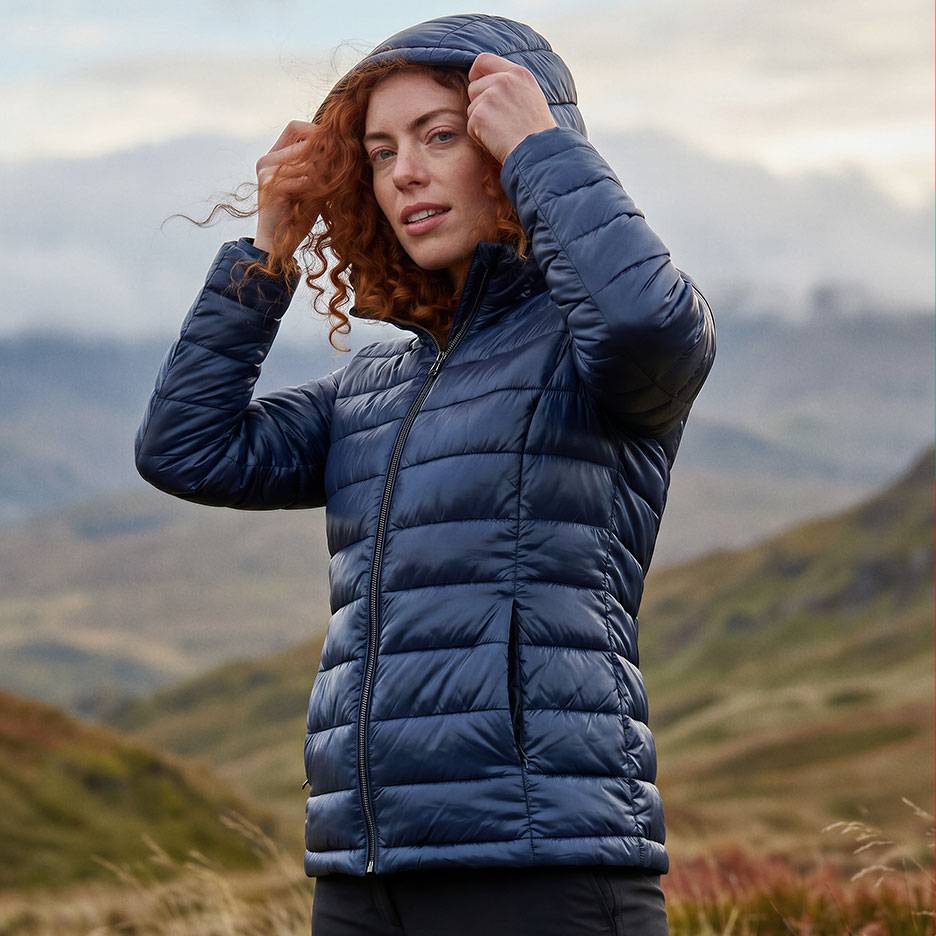 Woman with red hair in a dark blue hooded puffer jacket in a mountain landscape.