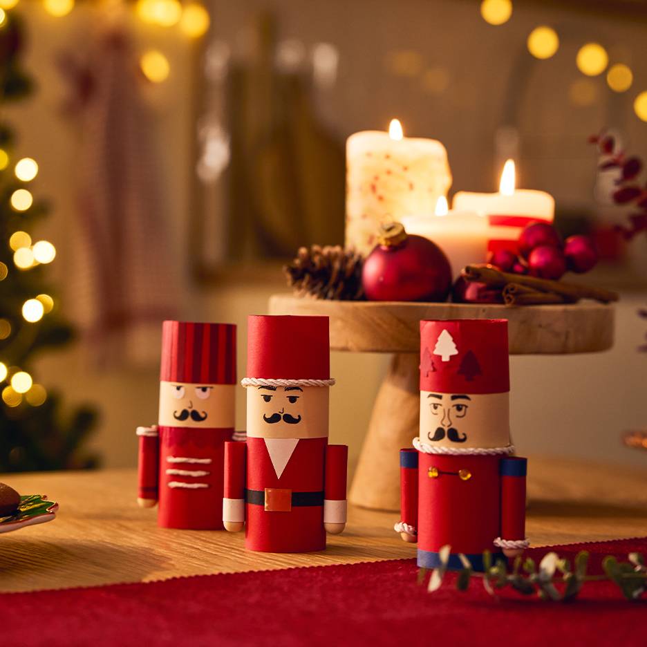 Three festive paper nutcrackers on a table with Christmas decorations and lit candles.