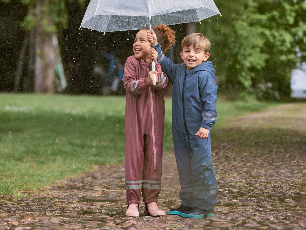 Two happy children in rain suits, under a transparent umbrella.