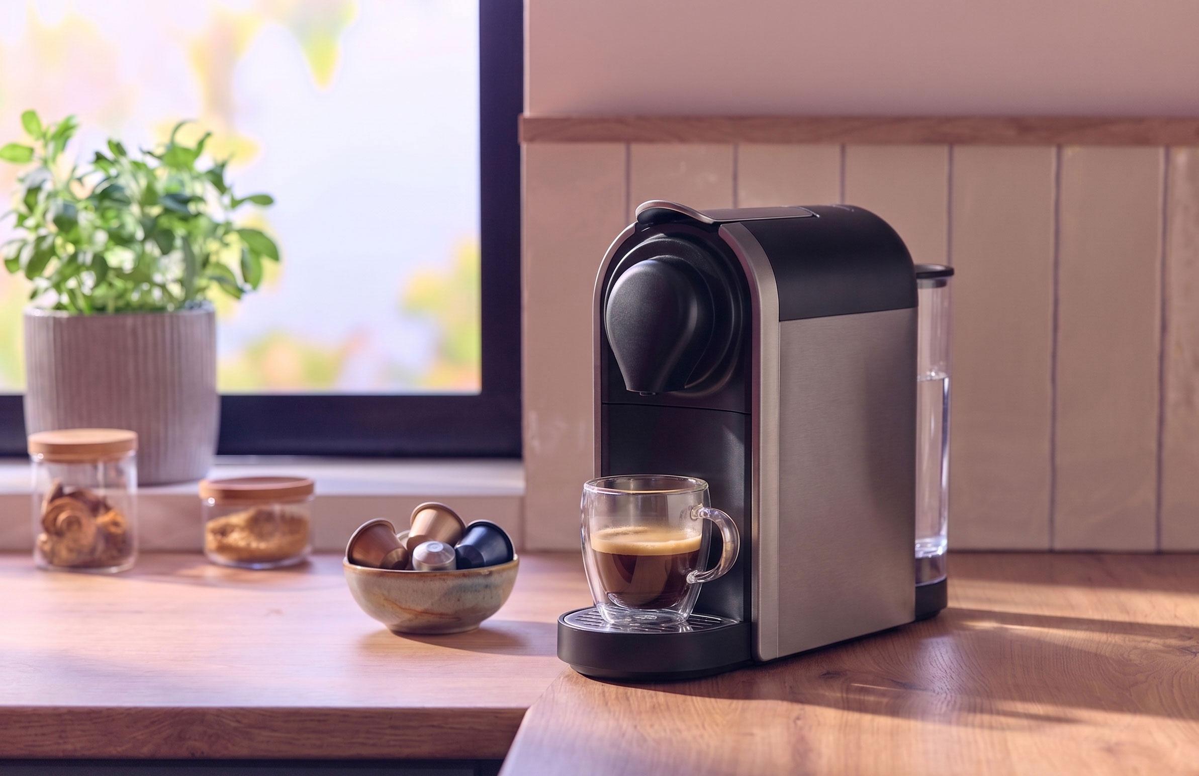 Coffee machine with a cup of coffee, capsules, and jars on a wooden counter.