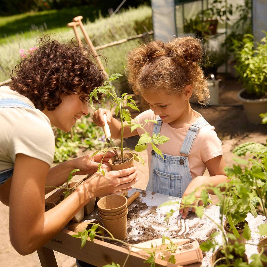 Mother and child planting seedlings in biodegradable pots, surrounded by gardening tools.