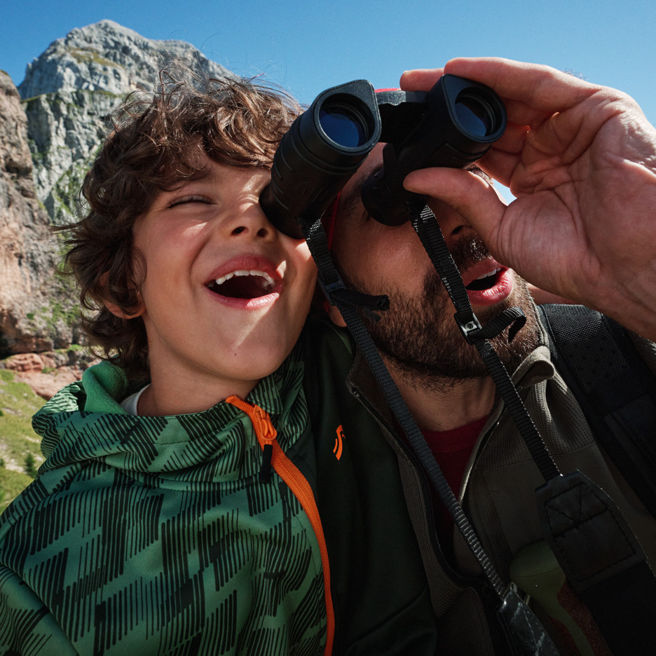 Father and son exploring mountains with binoculars, wearing outdoor jackets.