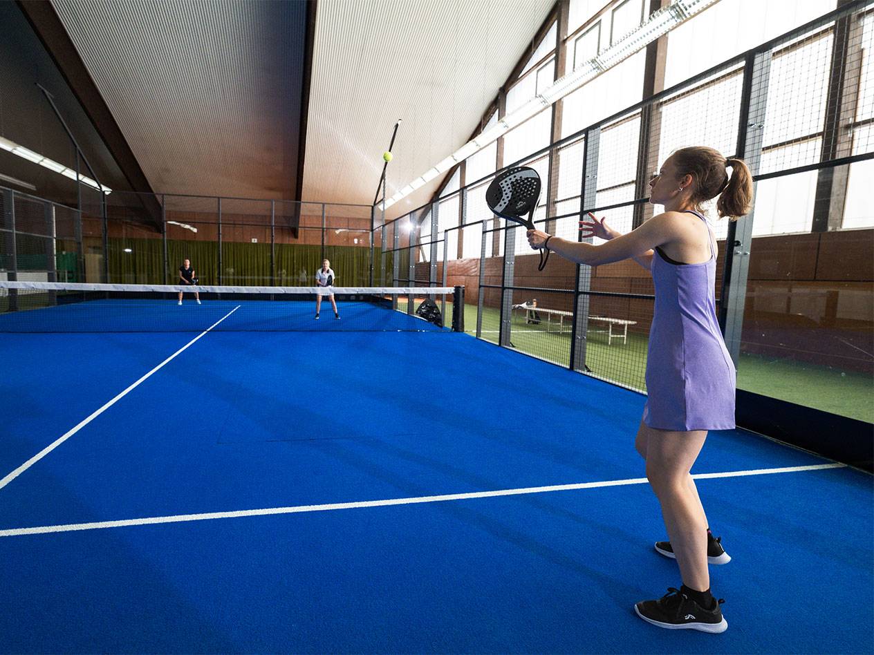 Woman in a purple dress playing padel on a blue court, holding a racket.