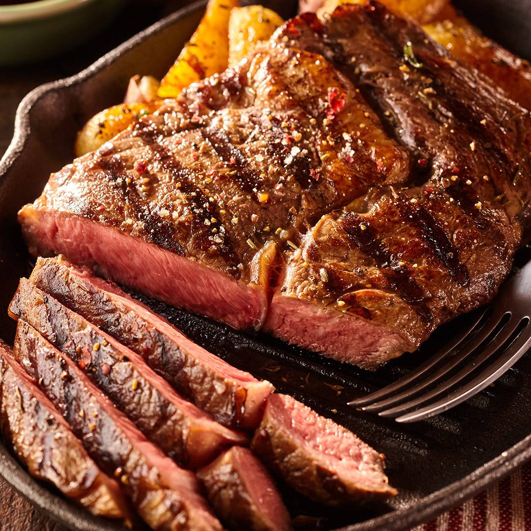 Sliced steak with roasted potatoes in a cast iron pan.