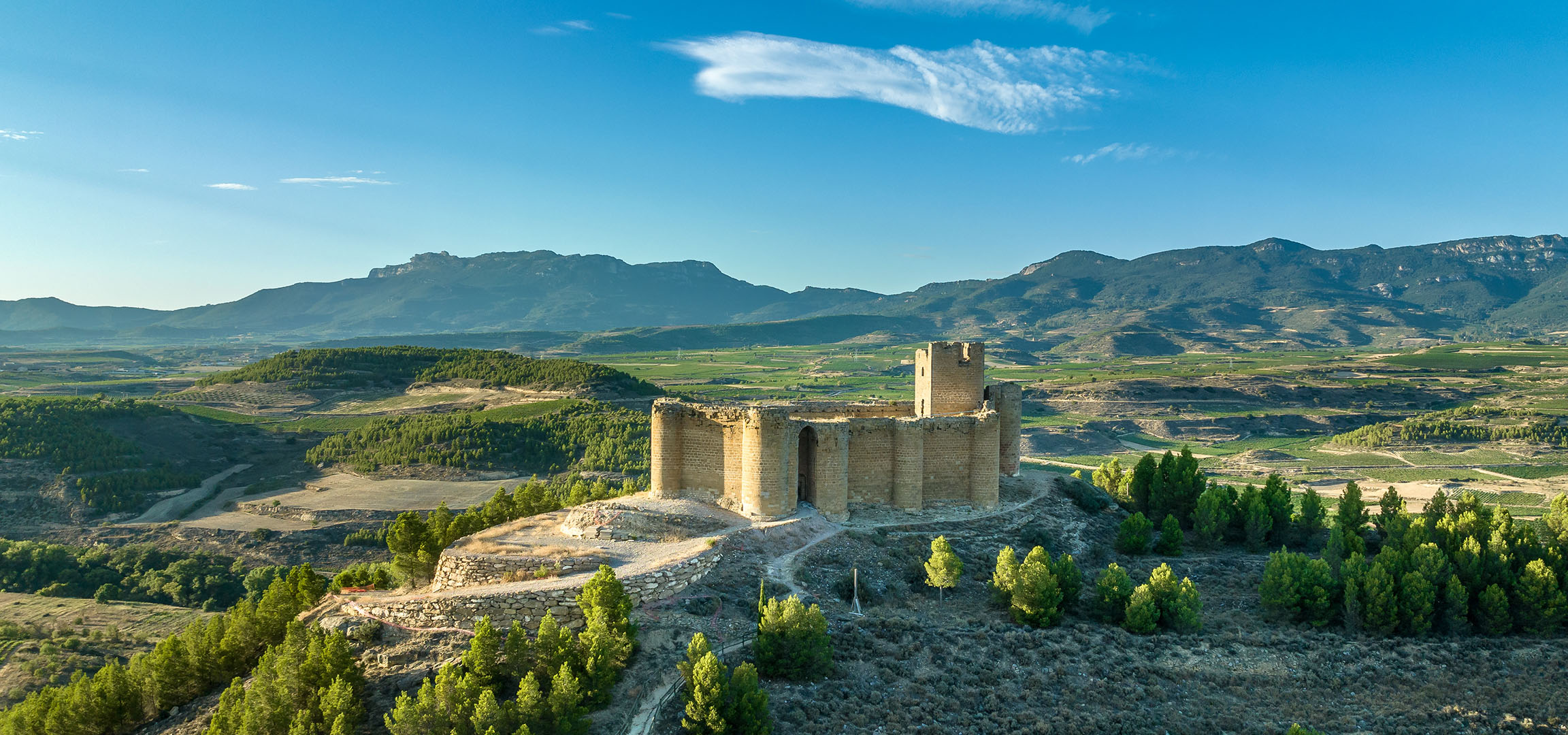 Ancient castle ruins on a hill overlooking a valley with vineyards and mountains.