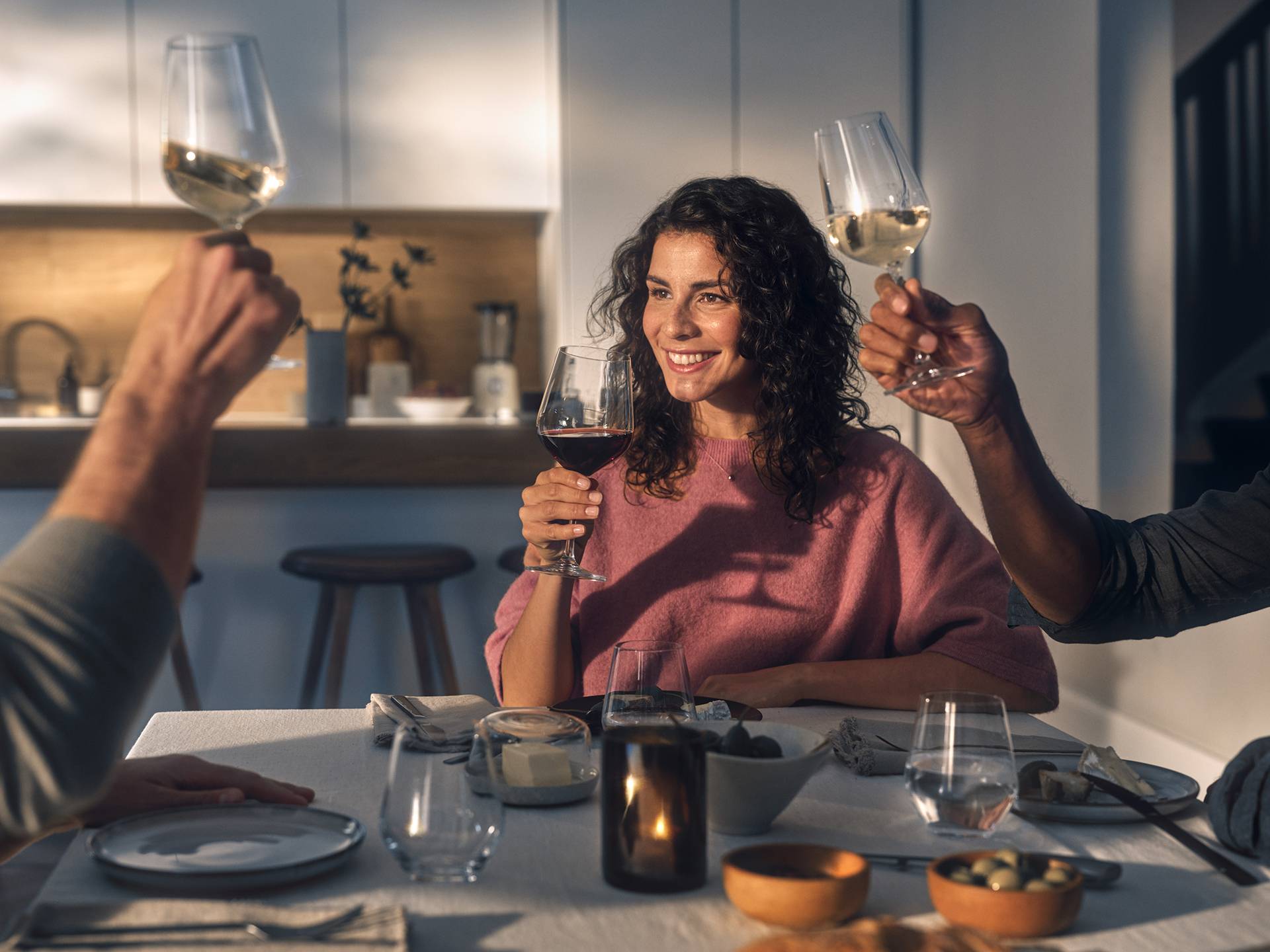 Friends toasting with wine glasses at a dinner table with food and candles.