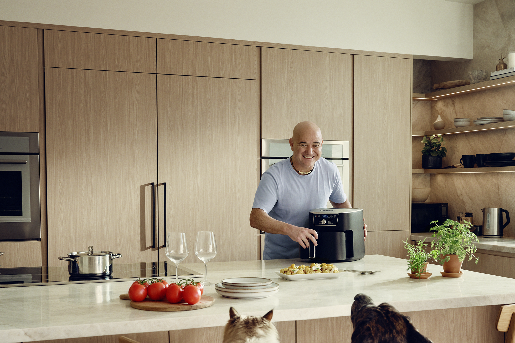 Man in kitchen with air fryer, preparing a meal while dogs watch.