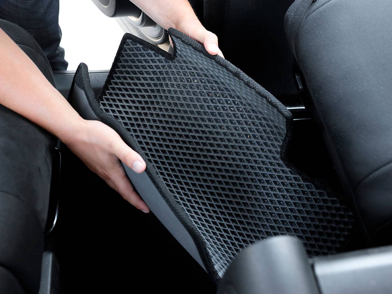 Person placing a black rubber car mat with a diamond pattern inside a vehicle.
