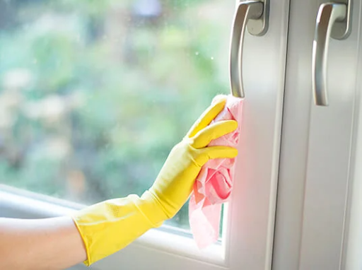 Hand in yellow glove wiping a window with a pink cloth.