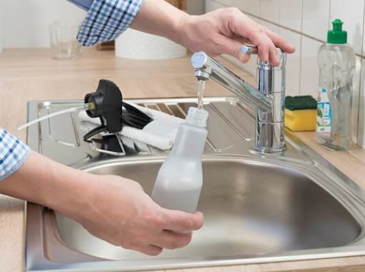 A person fills a spray bottle with water from a kitchen tap.