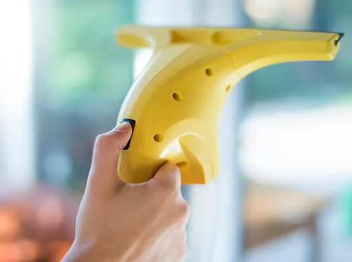 Hand holding a yellow electric window cleaner, cleaning a window.