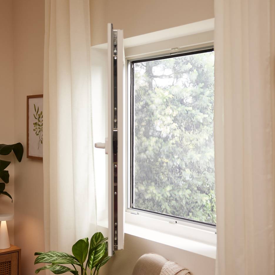 Open window with a mosquito net, white curtains, and indoor plants.