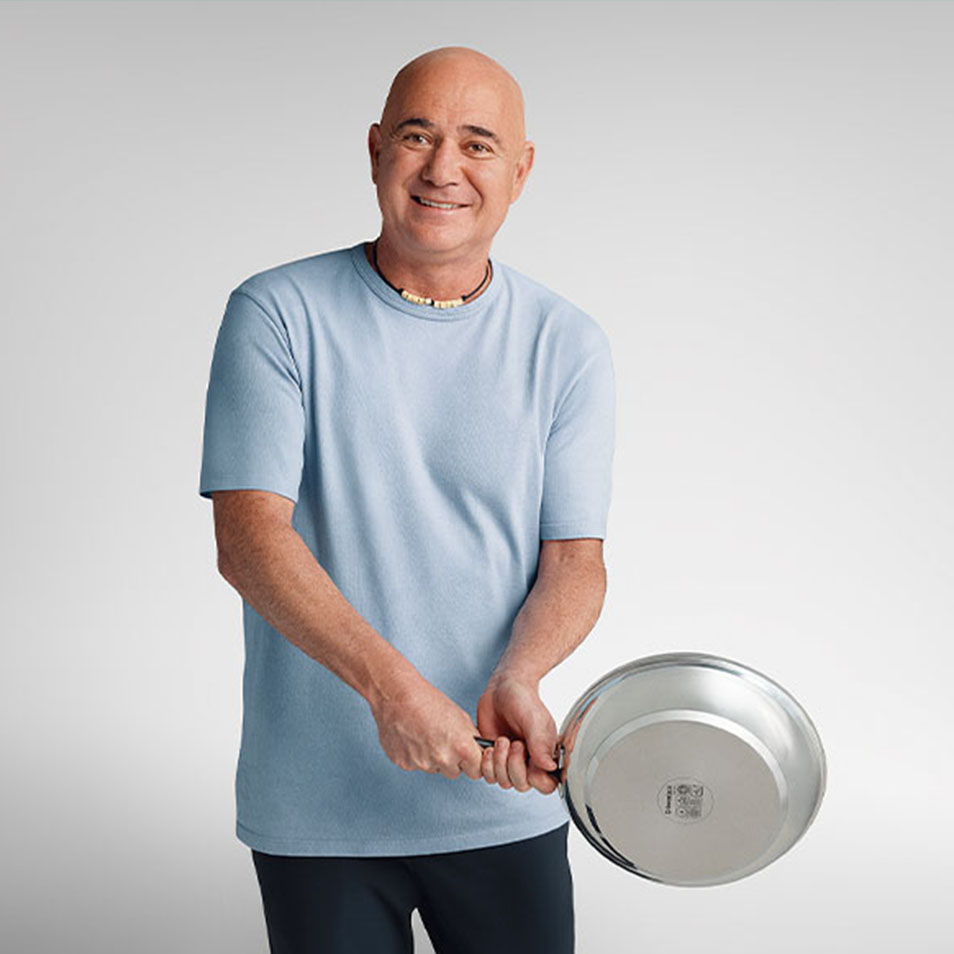 Man in light blue T-shirt holds a stainless steel pan and smiles.