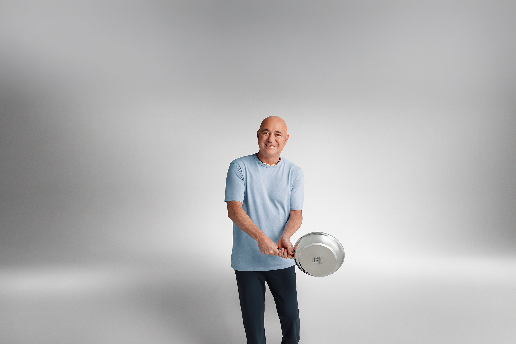 Man in a blue t-shirt holds a frying pan and smiles.