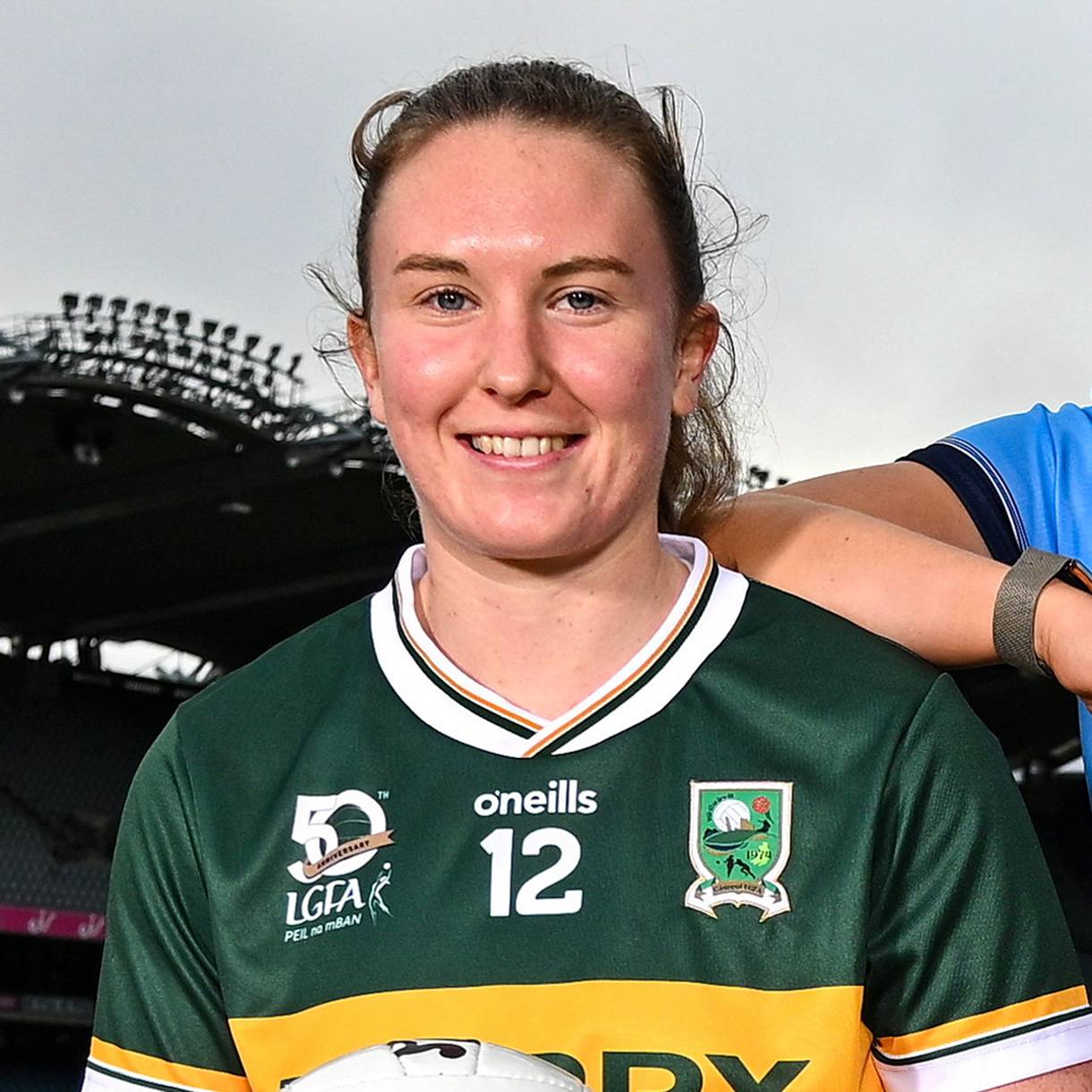 Smiling female athlete in a green and yellow jersey with number 12, holding a football.
