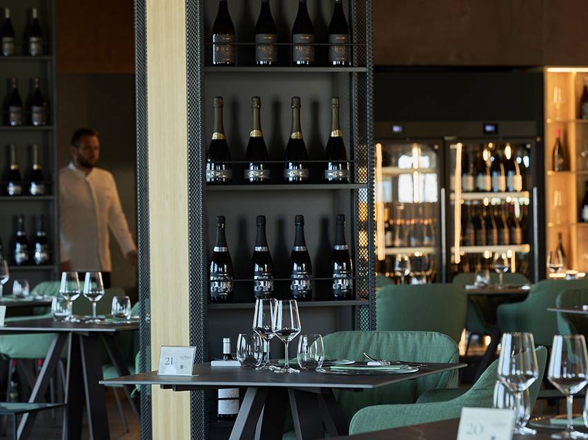 Restaurant interior with wine bottles on shelves and tables set with glasses.
