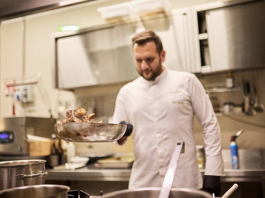 A chef in a white chef's jacket tossing food in a pan.