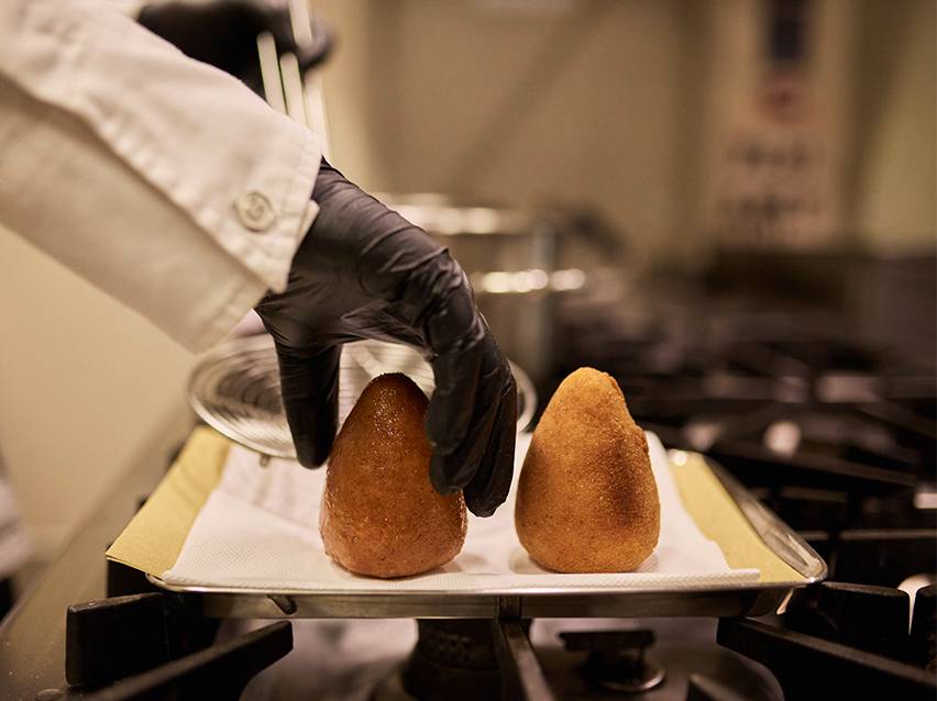 Chef in black gloves placing fried arancini on a tray with paper towels.