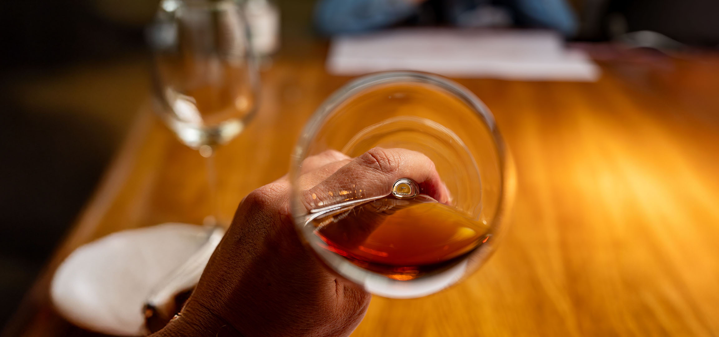 Close-up of a hand holding a glass of amber liquid, possibly whiskey or brandy.